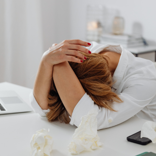 Blonde woman in white shirt with her head down on her desk in surrender and frustration